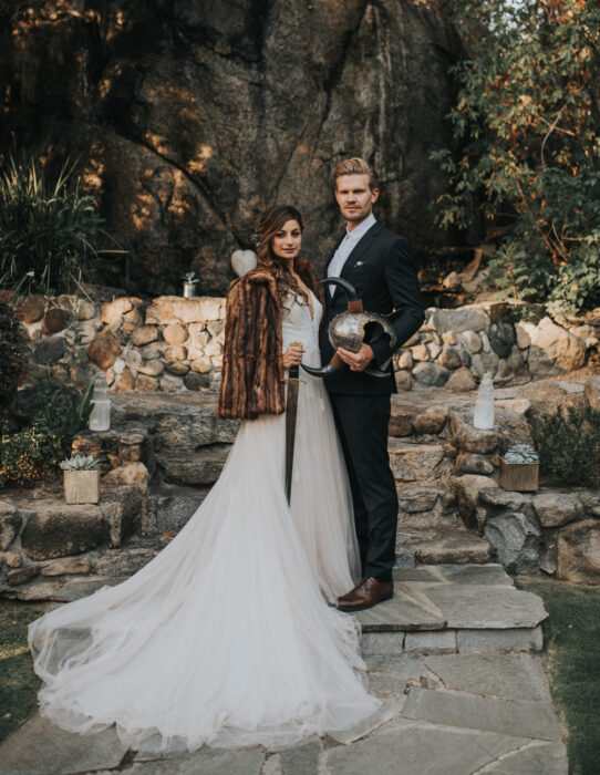 Ideas para una boda vikinga; novios, esposos en el bosque con vestido blanco y largo y traje negro, con casco con de cuernos