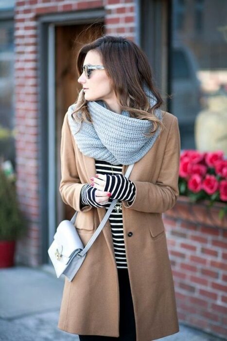 Chica usando bufanda larga de color gris, con blusa blanca con líneas negras, abrigo color camel