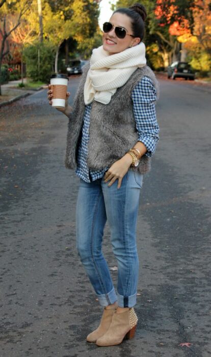 Chica usando bufanda larga de color beige, camisa de botones, chaleco de peluchito, jeans y botines 