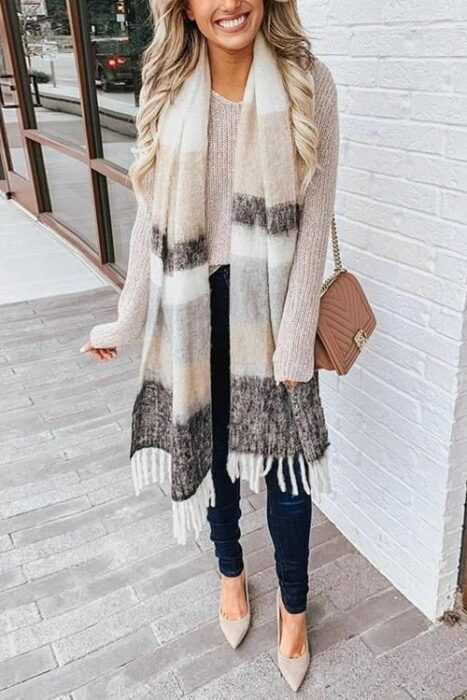 Chica usando bufanda larga de color neige, con líneas cafés y grises, suéter beige y jeans negros