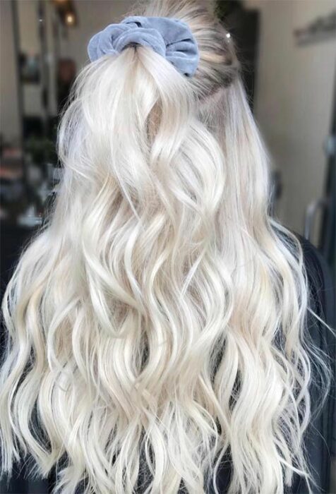 Chica de espaldas con cabello largo rizado en tono 'icy blonde' sujetado en media coleta con un scrunchie azul pastel