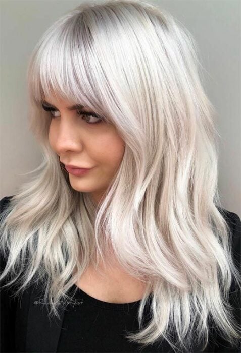 Chica con blusa negra mirando hacia un costado con melena larga cortada en capas cortas con tono de cabello blanco 'icy blonde' 