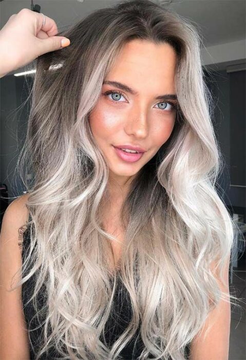 Chica de ojos verdes claros y labios rosas con blusa de tirantes negra y cabello largo degradado en café en la parte superior a blanco 'icy blonde' de medios a puntas