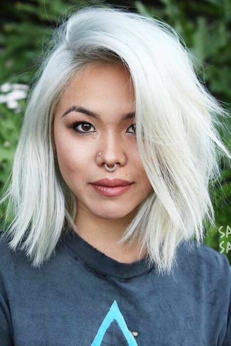 Chica asiática con cabello corto en capas el color blanco 'icy blond' vistiendo blusa azul marino con un septum en la nariz 