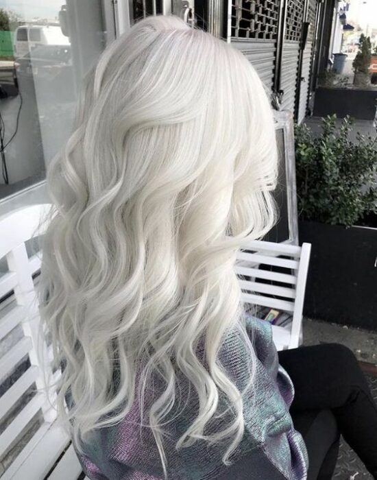 Chica sentada de espaldas con cabello largo rizado en tono 'icy blonde'