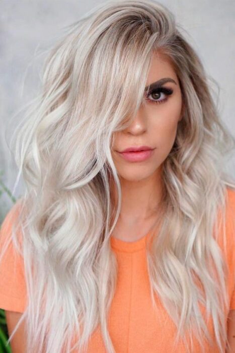 Chica con blusa naranja con cabello largo rizado en tono 'icy blond'