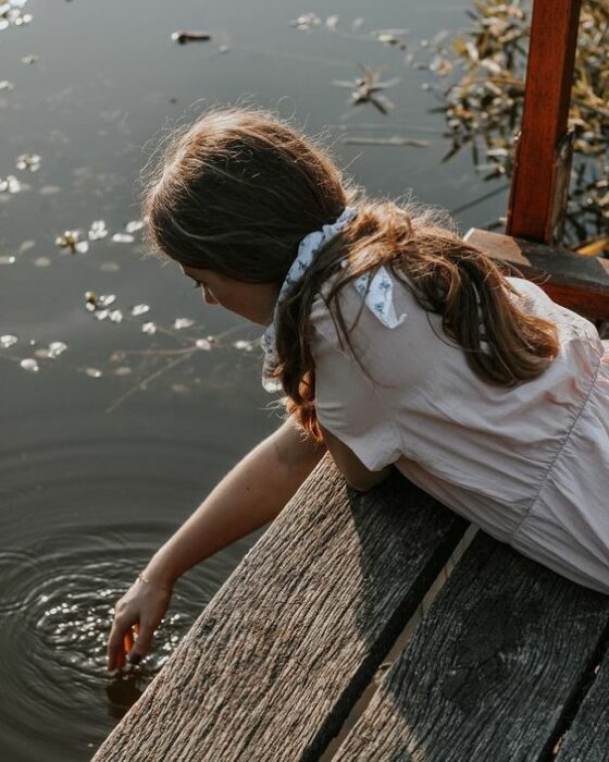 Chica tocando al agua de un lago con la mano