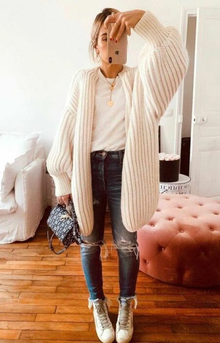 Chica usando cardigan largo color perla, blusa blanca y jeans rasgados con botines blancos