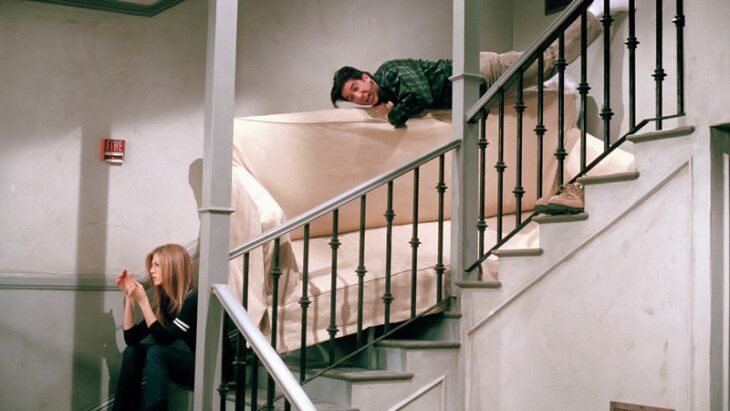 RACHEL Y ROSS de friends en las escaleras de un edificio tratando se bajar un sillón beigr