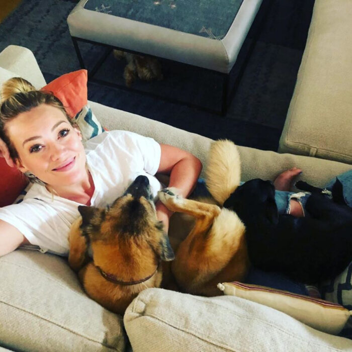 Famosos que han adoptado mascotas, perros o gatos; Hilary Duff sentada en el sillón con sus perritas Lucy y MoMo, color negro y café