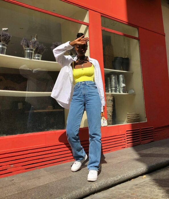 Chica usando unos jeans y top de color amarillo con una camisa de botones color blanca sobre él