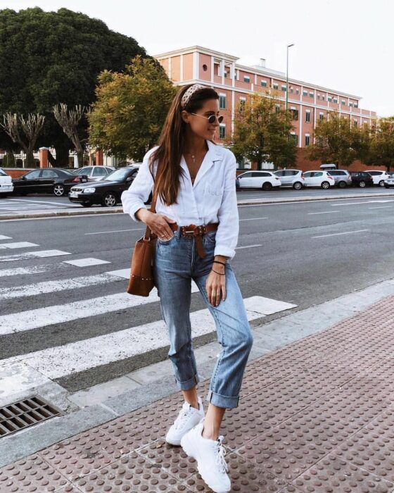 Chica usando una camisa de color blanco con botones y jeans junto con tenis 