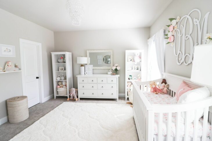 Habitación de un bebé decorada con muebles en color blanco con una cuna, cambiador y una repisa para acomodar juguetes 