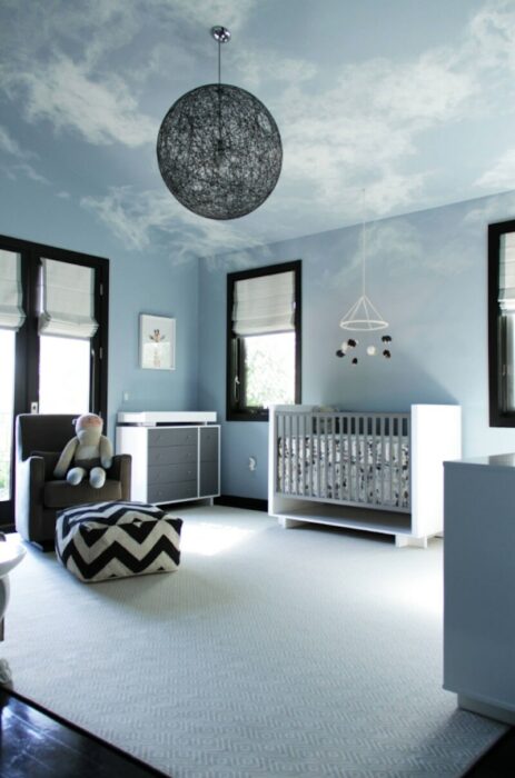 Habitación para un bebé decorada en tonos azules con un sofá, cuna y una lámpara en forma de luna 