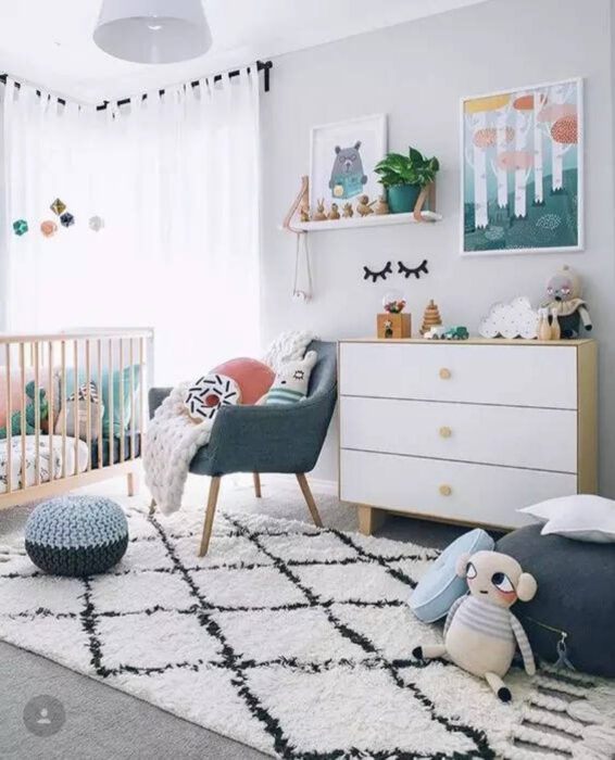 Habitación para un bebé con muebles en color azul, cuna de madera, cajonera de color blanco y diferentes juguetes regados por el lugar 