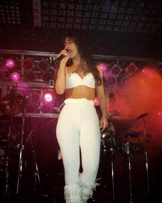 Selena Quintanilla usando un outfit de color blanco con botas de lentejuela y bustie blanco