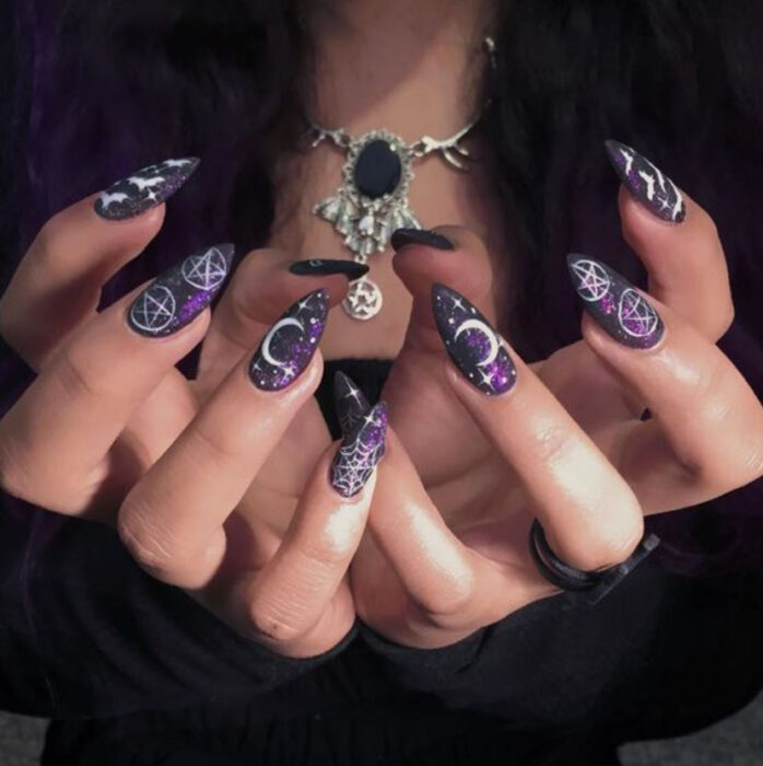 Manicura inspirada en noche de brujas de fondo color negro con morado con detalles en color blanco