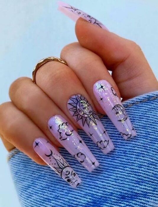 Manicura de acrílico estilo aesthetic de fondo lila con diseño en negro de soles, nubes y estrellas