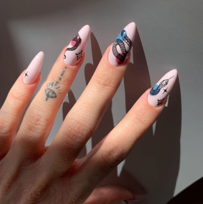 Manicura de acrílico estilo aesthetic de fondo rosa bebé con diseño de serpiente a mano alzada a lo largo de todas las uñas