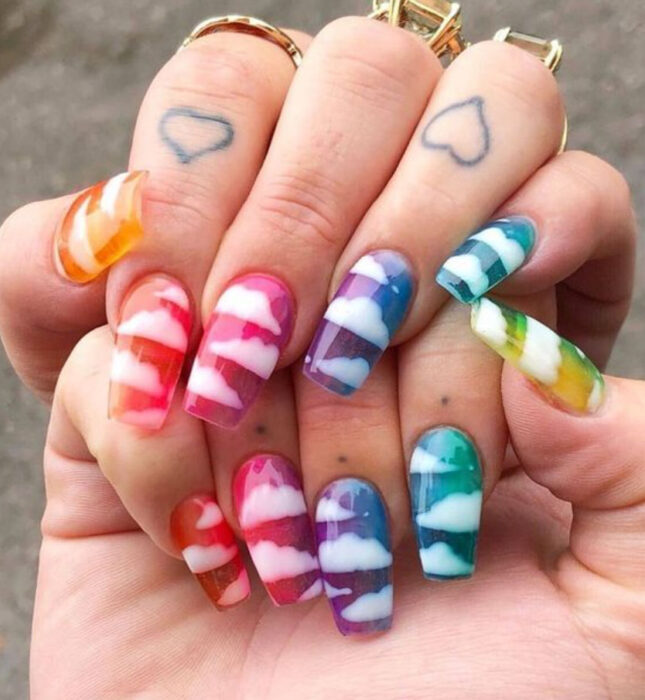 Manicura de acrílico estilo aesthetic de colores rosas, moradas, verdes, amarillas con diseño de nubes en color blanco