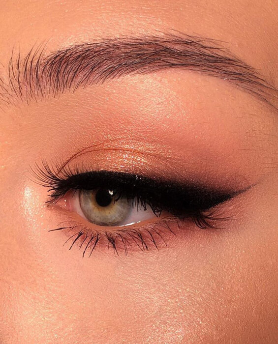 Chica con un maquillaje de ojos en color dorado con un cat eye negro y grande 