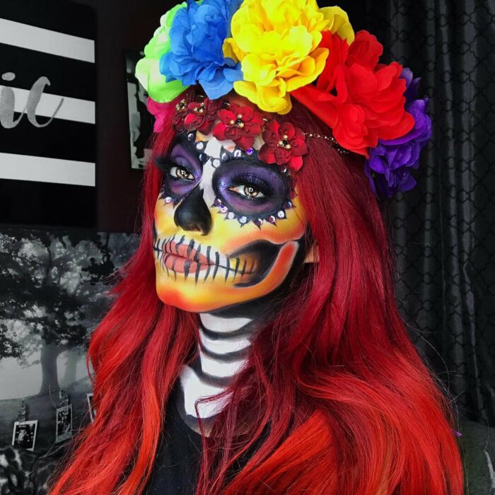 Chica con un maquillaje de catrina en colores rojos con morado y amarillo 