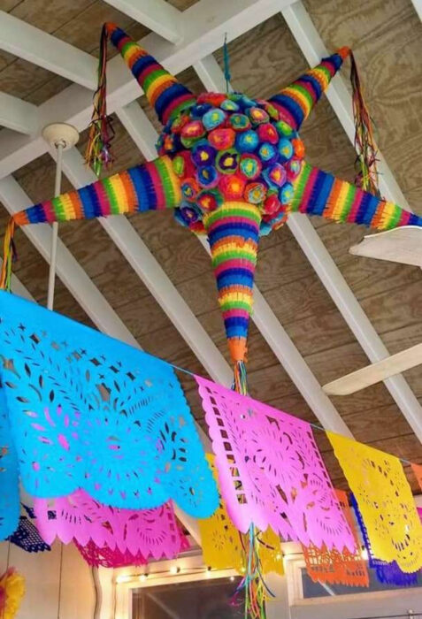 Decoración de Navidad con temática mexicana; piñata de estrella de colores anaranjado, azul, rojo, verde, amarillo y papel picado