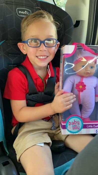 Niño sentado en el asiento de un coche sosteniendo una muñeca que pidió de regalo