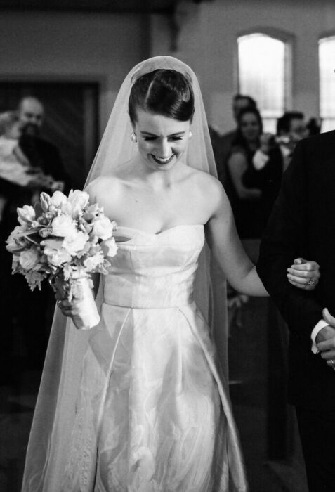 Fotografía blanco y negro de novia caminando al altar con vestido de novia strapless 