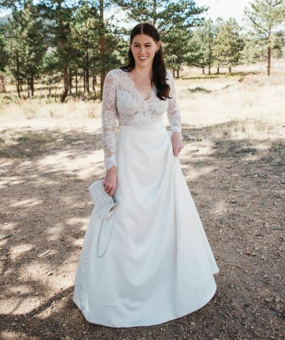 Novia con media coleta usando un vestido con la parte superior de encaje con escote en V y la falda de satín larga