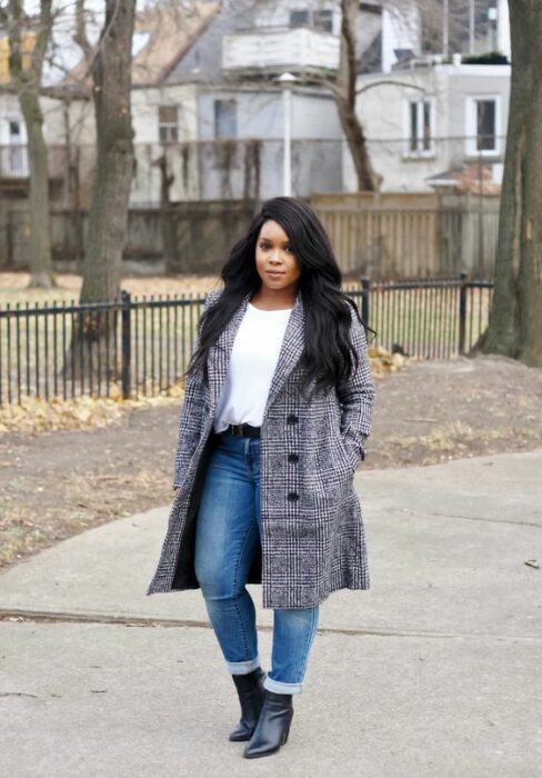 Chica curvy usando jeans, botines negros, blusa blanca y abrigo gris de cuadros