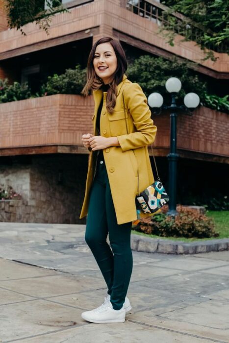 Outfit para la oficina de otoño-invierno de abrigo color moztaza, blusa y pantalón color petroleo y tenis blancos