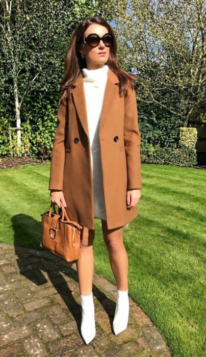 Chica usando botines blancos y vestido blanco corto con abrigo color camel 