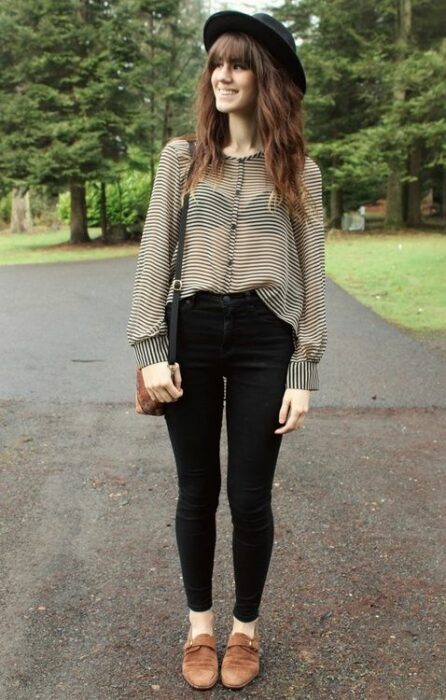 Chica usando sombrero de color negro con outfit de mocasín camel, jeans negros y blusa de gaza de color blanco con lunares negros