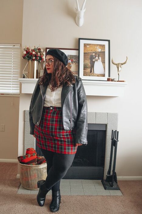 Chica curvy usando botines y mallas negras, falda roja a cuadros, blusa blanca y saco gris y una boina negra