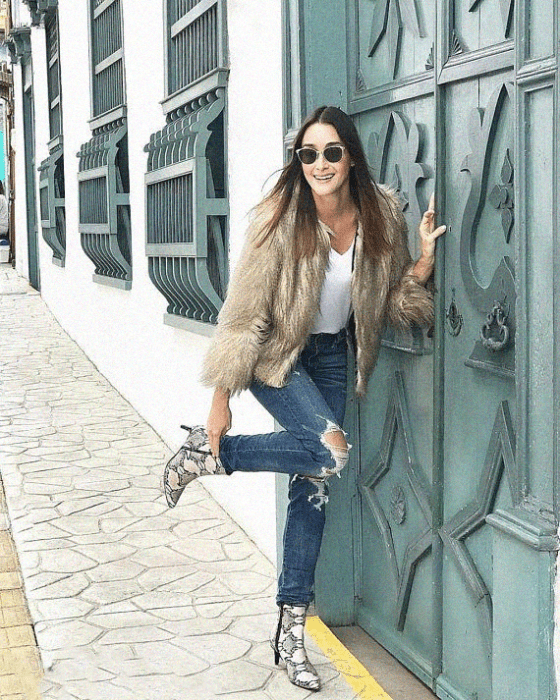 Chica usando botas pitón con jeans rasgados, blusa blanca y saco estilo furry