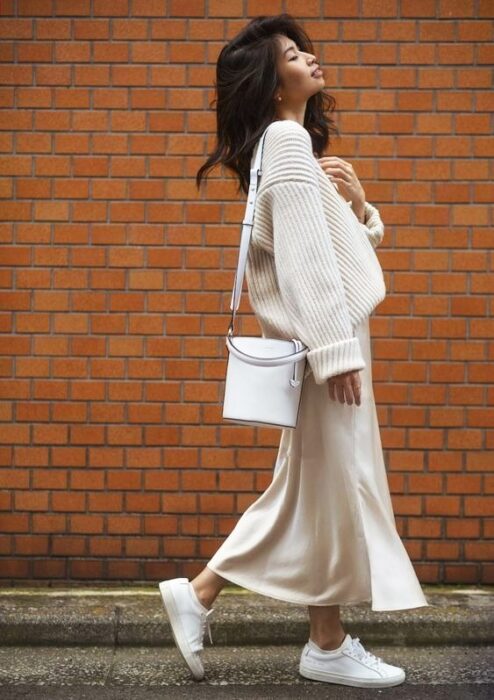 Chica usando un total white look de tenis, falda larga y suéter holgado