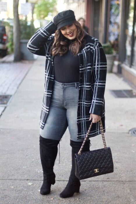Chica curvy usando botas largas, jeans, blusa gris y abrigo de cuadros 