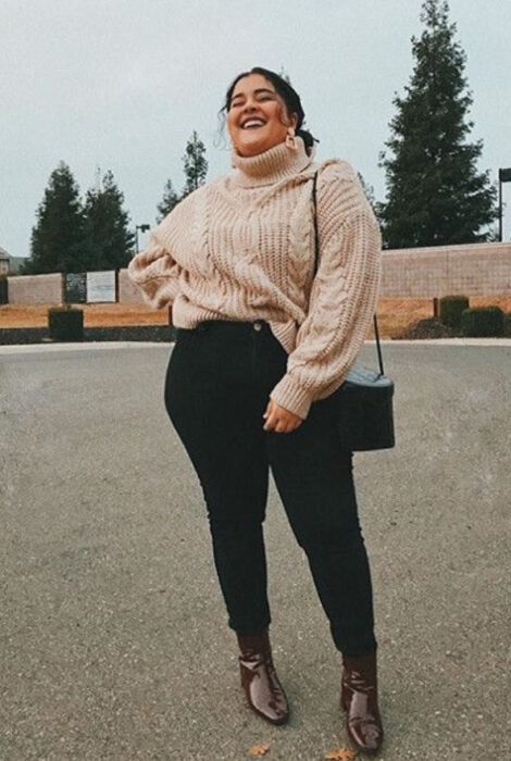 Chica curvy usando jeans negros, botines cafés y suéter de cuello de tortuga color rosa coral