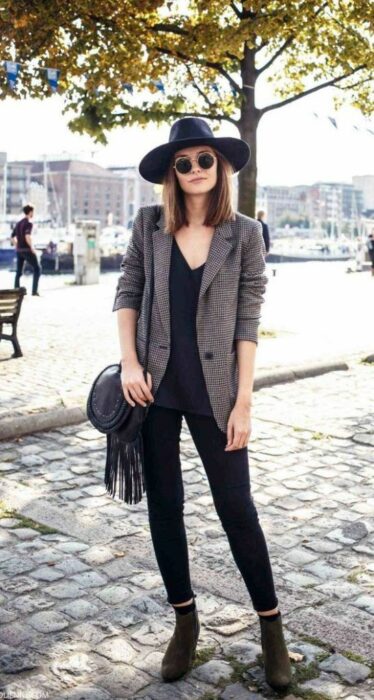 Chica usando sombrero de color negro con outfit de botines, jeans y blusa negra y blazer gris