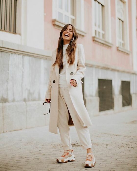 Chica usando un total white look de tenis, pantalón de vestir, blusa y abrigo largo