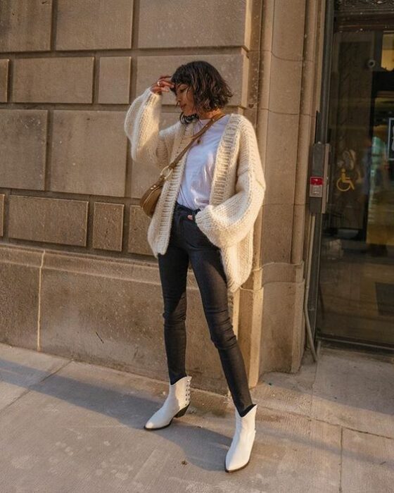 Chica usando botines blancos y jeans deslavados negros, blusa blanca y suéter holgado beige