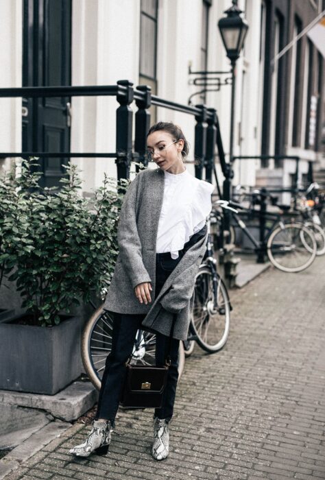 Chica usando botas pitón con pantalón de vestir negro, blusa blanca y blazer gris, con bolsa de mano color negra 