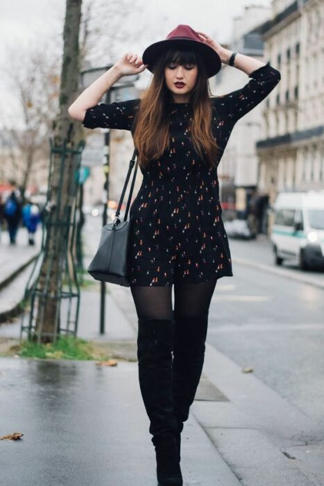 Chica usando sombrero de color guinda con outfit de medias y botines negros y vestido negro con lunares blancos