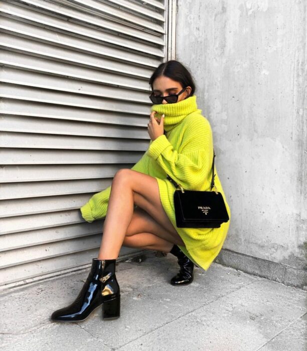 Chica usando un suéter oversized de color verde neón con unos botines de color negro 