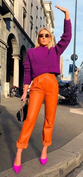 Chica usando un pantalón de color naranja combinado con un suéter de color morado y zapatos del mismo color 