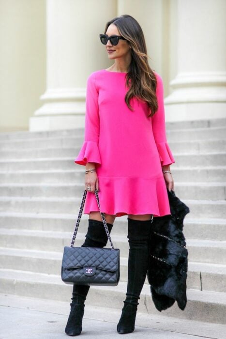 Chica usando un vestido de color rosa con botas altas y chaqueta 