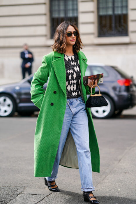 Chica usando un abrigo largo de color verde con un suéter de rombos y  jeans 