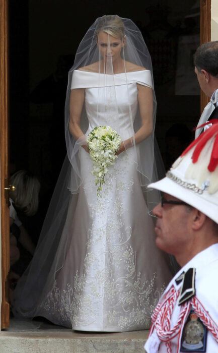 Charlene de mónaco el día de su boda luciendo un vestido blanco de encaje con un ramo de novia con flores blancas 