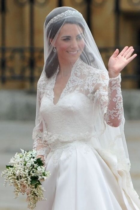 Kate Middleton  el día de su boda luciendo un vestido blanco de encaje con un ramo de novia con flores blancas 